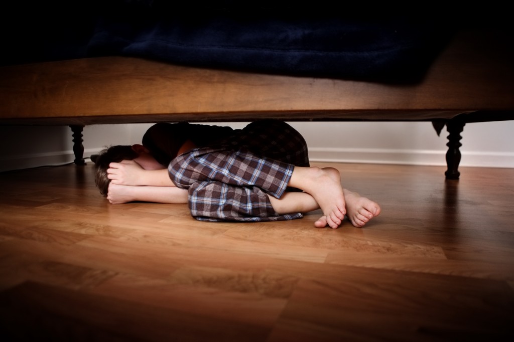 Fearful boy hiding under the bed